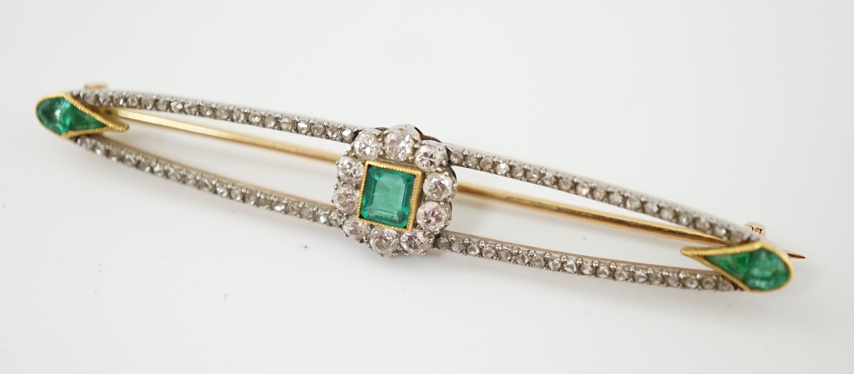 A Belle Epoque gold and platinum, emerald and round cut diamond cluster set elliptical bar brooch